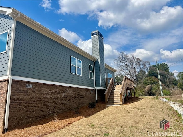 view of home's exterior featuring stairs, a chimney, brick siding, and a wooden deck