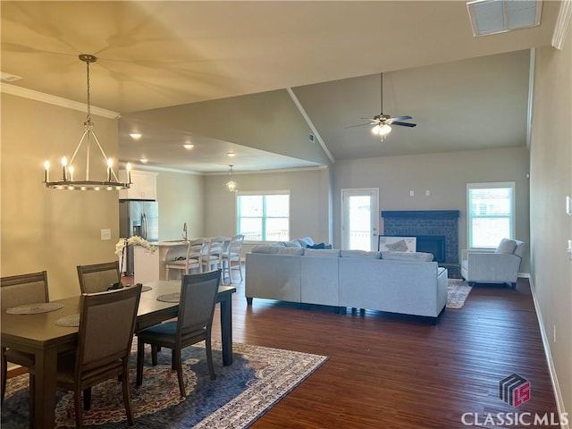 dining space with visible vents, crown molding, vaulted ceiling, ceiling fan with notable chandelier, and dark wood-style floors