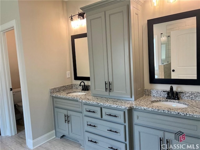 bathroom featuring a sink, baseboards, toilet, and double vanity