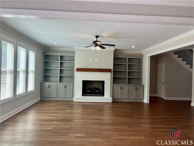 unfurnished living room featuring stairway, a ceiling fan, wood finished floors, baseboards, and crown molding