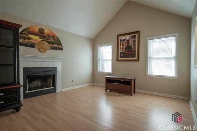 unfurnished living room featuring lofted ceiling, light wood-style flooring, baseboards, and a tile fireplace