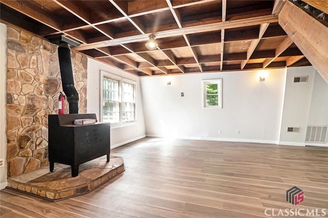 living area with a wealth of natural light, visible vents, a wood stove, and wood finished floors