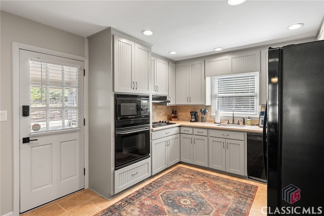 kitchen with under cabinet range hood, plenty of natural light, black appliances, and a sink