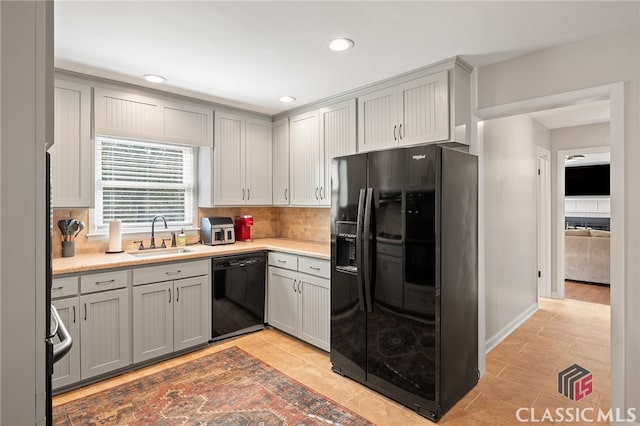 kitchen with decorative backsplash, black appliances, light countertops, and a sink