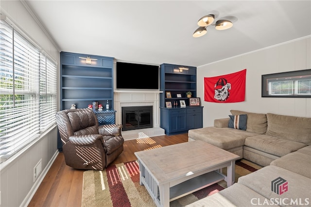 living room with built in features, wood finished floors, visible vents, ornamental molding, and a brick fireplace