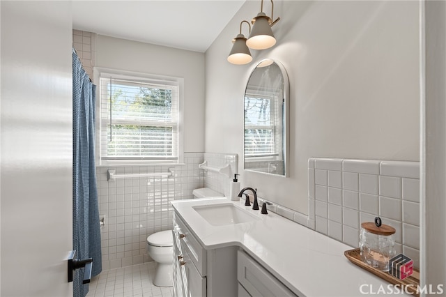 full bath featuring tile patterned flooring, toilet, vanity, wainscoting, and tile walls