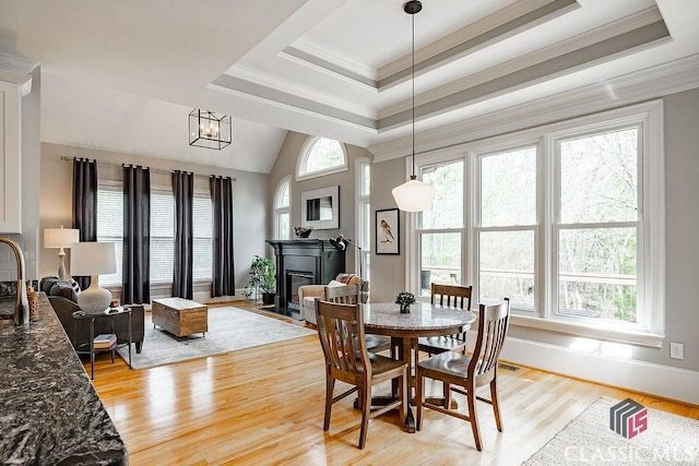 dining space with a fireplace with flush hearth, a raised ceiling, light wood-style floors, and ornamental molding