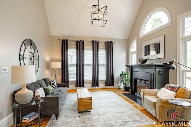 living area featuring a glass covered fireplace, high vaulted ceiling, an inviting chandelier, and wood finished floors