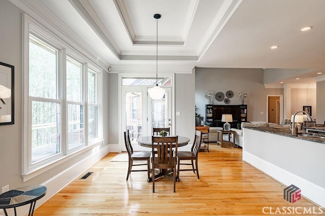 dining area with a tray ceiling, light wood-style floors, visible vents, and ornamental molding