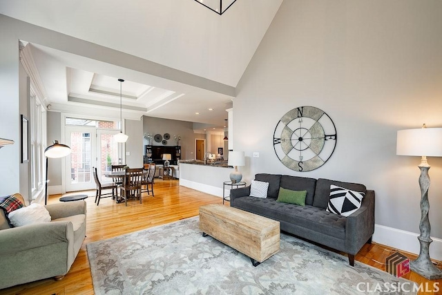 living room with a tray ceiling, light wood-type flooring, baseboards, and a towering ceiling