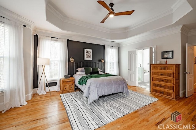 bedroom with a raised ceiling, light wood-style flooring, and multiple windows