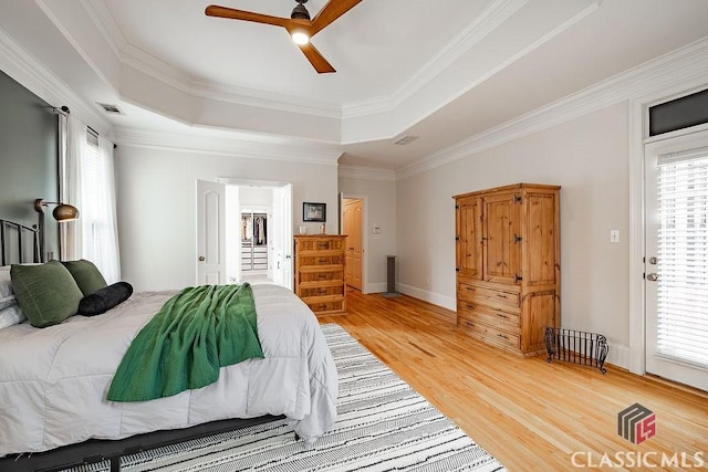 bedroom featuring visible vents, ornamental molding, a tray ceiling, light wood-style floors, and ceiling fan