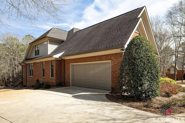 view of side of property with a garage, brick siding, roof with shingles, and driveway