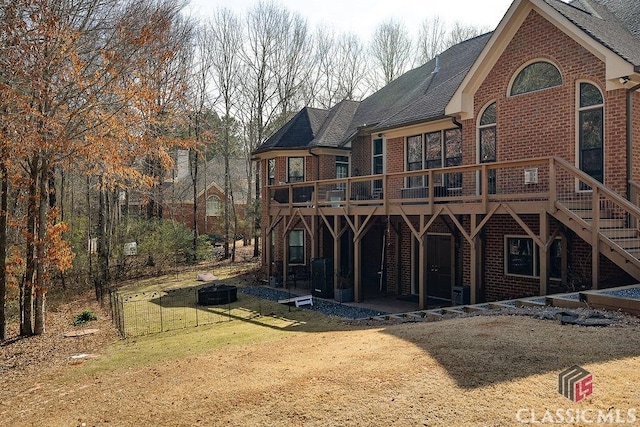 rear view of property with a patio, a yard, roof with shingles, a wooden deck, and brick siding