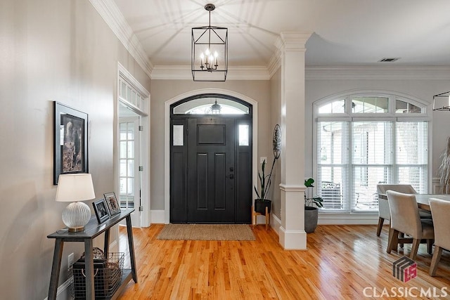 foyer with light wood finished floors, visible vents, baseboards, a chandelier, and ornamental molding