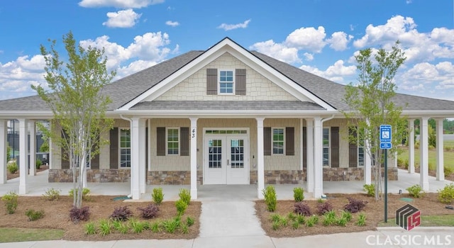 view of front of property featuring stone siding, covered porch, french doors, and a shingled roof