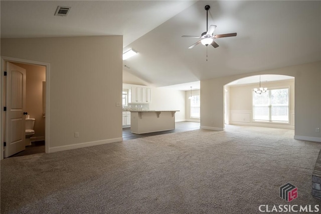 unfurnished living room featuring arched walkways, dark carpet, ceiling fan with notable chandelier, and plenty of natural light
