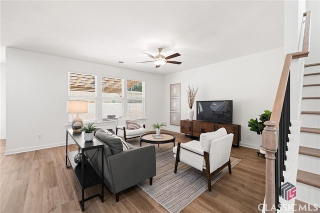 living area featuring a ceiling fan, stairway, light wood finished floors, and baseboards