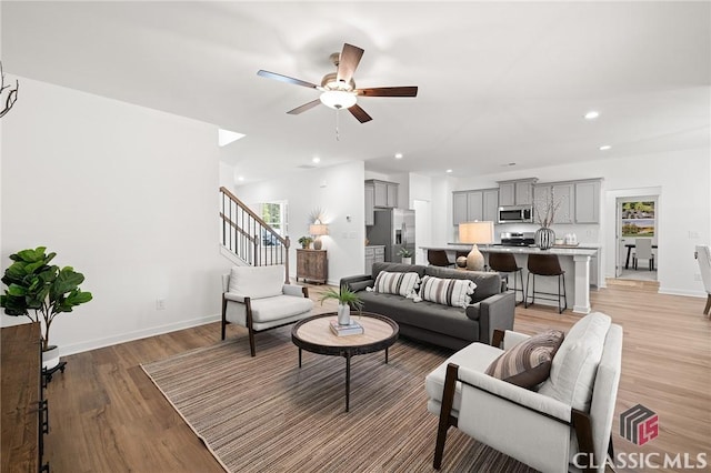 living room with a ceiling fan, stairway, baseboards, light wood-style floors, and recessed lighting
