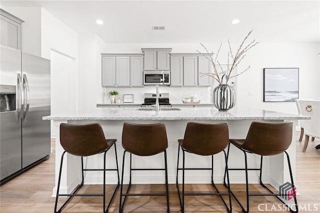 kitchen featuring an island with sink, gray cabinetry, a kitchen bar, and appliances with stainless steel finishes