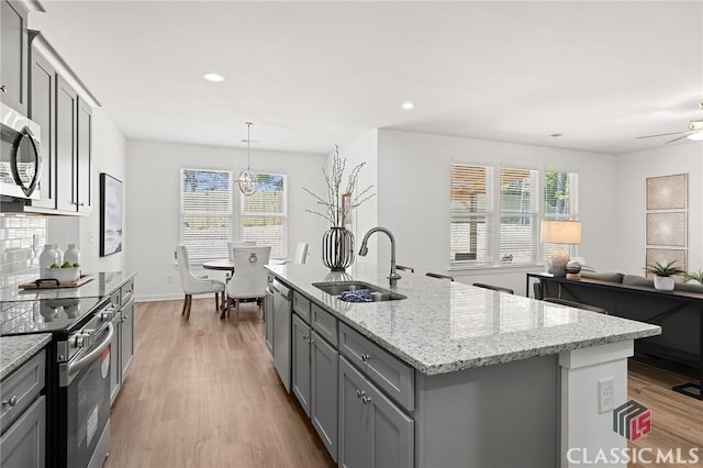 kitchen featuring a sink, a kitchen island with sink, light wood-style flooring, gray cabinetry, and appliances with stainless steel finishes