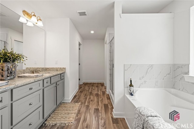bathroom with a garden tub, wood finished floors, a stall shower, visible vents, and vanity