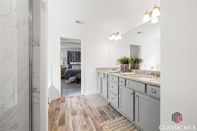 full bathroom with ensuite bathroom, visible vents, a sink, double vanity, and wood finished floors