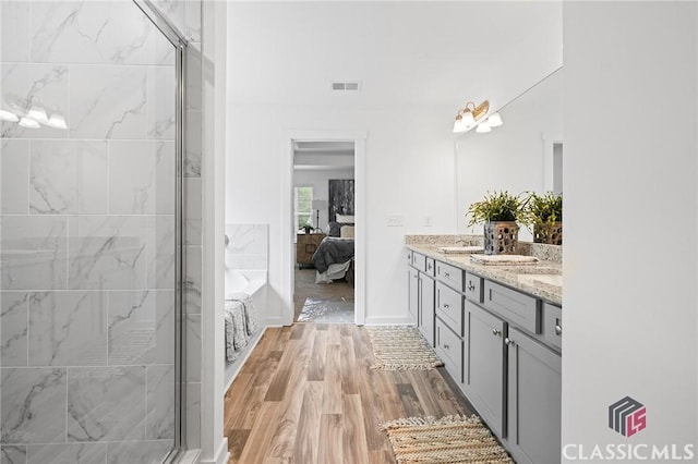 ensuite bathroom with double vanity, ensuite bathroom, wood finished floors, and a shower stall