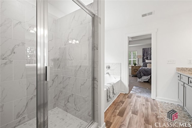 ensuite bathroom with a stall shower, ensuite bath, visible vents, and wood finished floors