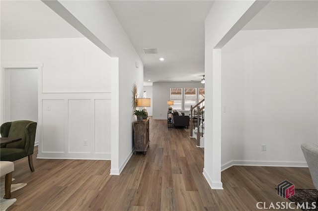 hall featuring a decorative wall, wood finished floors, visible vents, recessed lighting, and stairway