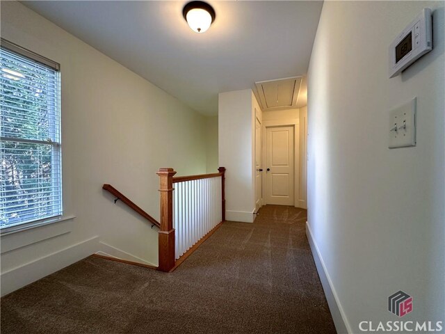corridor with attic access, baseboards, an upstairs landing, and dark colored carpet