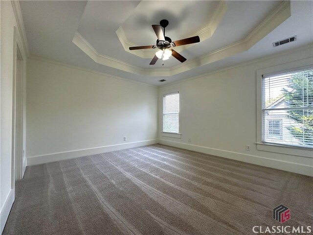 carpeted empty room with baseboards, ornamental molding, visible vents, and a raised ceiling