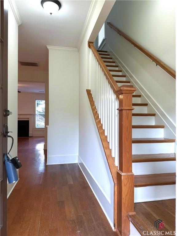 staircase with ornamental molding, baseboards, hardwood / wood-style flooring, visible vents, and a fireplace
