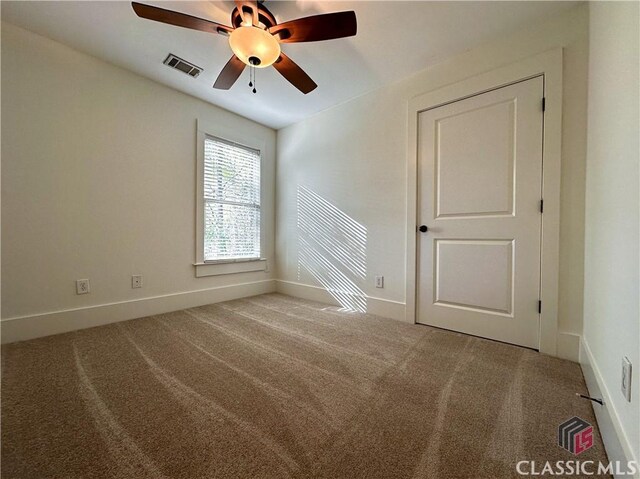 carpeted spare room featuring baseboards, visible vents, and a ceiling fan