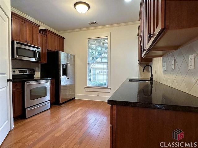 kitchen featuring a sink, light wood finished floors, stainless steel appliances, decorative backsplash, and ornamental molding
