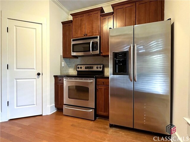 kitchen with crown molding, stainless steel appliances, dark countertops, light wood-style floors, and decorative backsplash