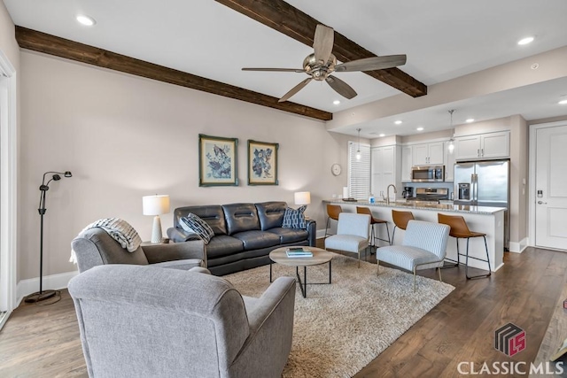 living room featuring baseboards, beamed ceiling, wood finished floors, and a ceiling fan