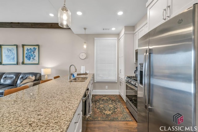 kitchen with a sink, light stone countertops, appliances with stainless steel finishes, dark wood finished floors, and white cabinets