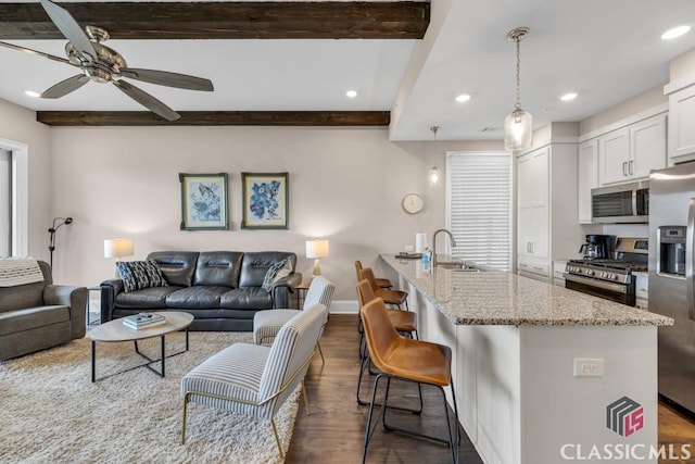 kitchen featuring open floor plan, a sink, appliances with stainless steel finishes, and beamed ceiling