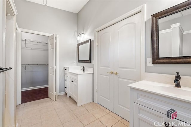 bathroom with a sink, two vanities, a walk in closet, and tile patterned flooring