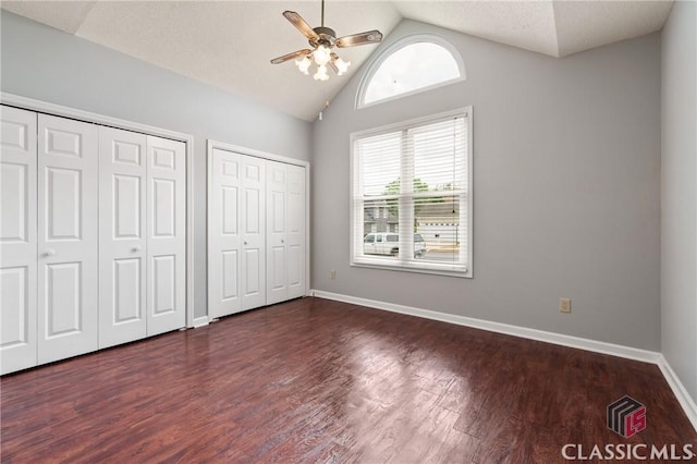 unfurnished bedroom with baseboards, dark wood-style floors, two closets, a ceiling fan, and lofted ceiling