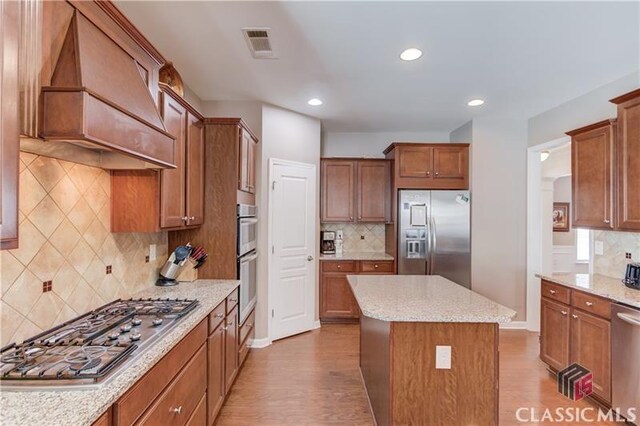 6706 Mill Rock Ct, Hoschton, GA 30548 - kitchen featuring visible vents, appliances with stainless steel finishes, a sink, brown cabinets, and custom range hood