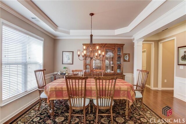 6706 Mill Rock Ct, Hoschton, GA 30548 - dining room featuring a raised ceiling, a chandelier, decorative columns, and wood finished floors