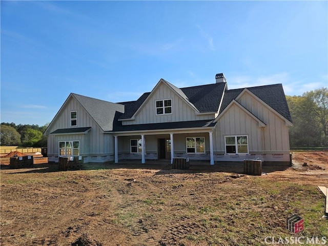 modern farmhouse featuring a chimney, cooling unit, board and batten siding, a porch, and a shingled roof