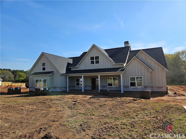 modern farmhouse featuring a chimney, board and batten siding, a porch, central AC unit, and a shingled roof