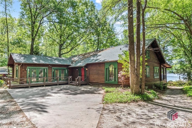 view of front of property featuring log siding, driveway, french doors, a wooden deck, and a shingled roof