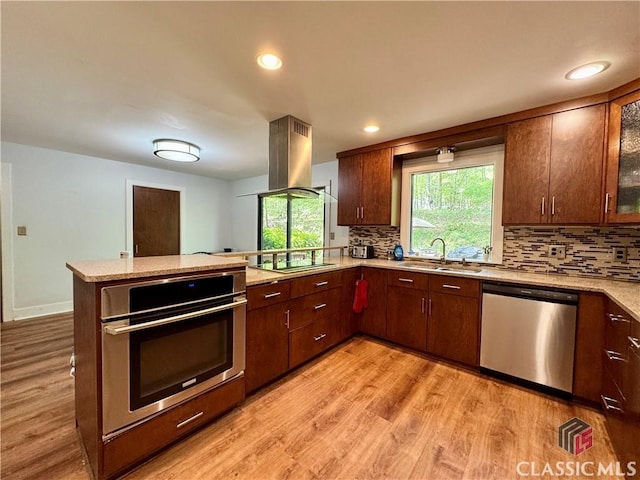 kitchen with backsplash, island exhaust hood, appliances with stainless steel finishes, and a sink