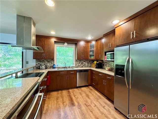kitchen featuring stainless steel appliances, light wood-style flooring, island exhaust hood, a sink, and decorative backsplash