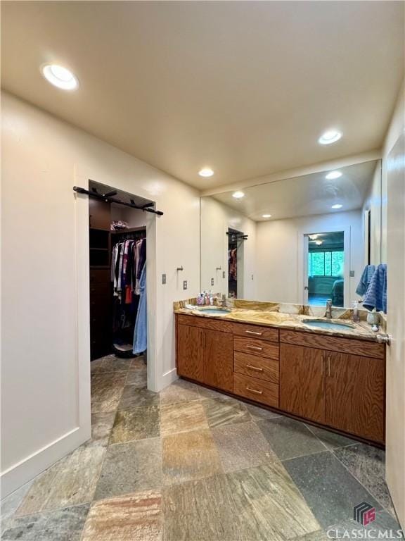 bathroom with baseboards, a sink, a spacious closet, and double vanity