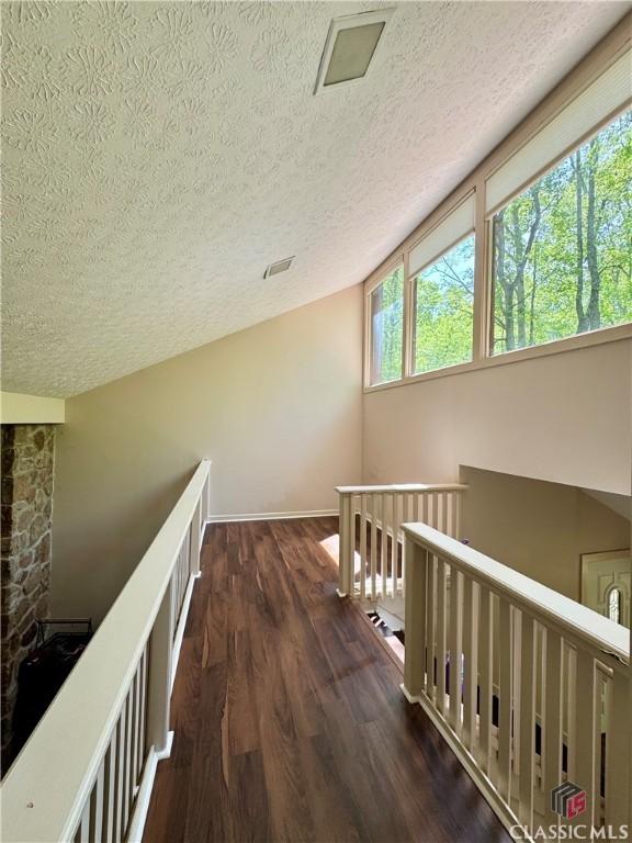hall featuring wood finished floors, a textured ceiling, a healthy amount of sunlight, and an upstairs landing